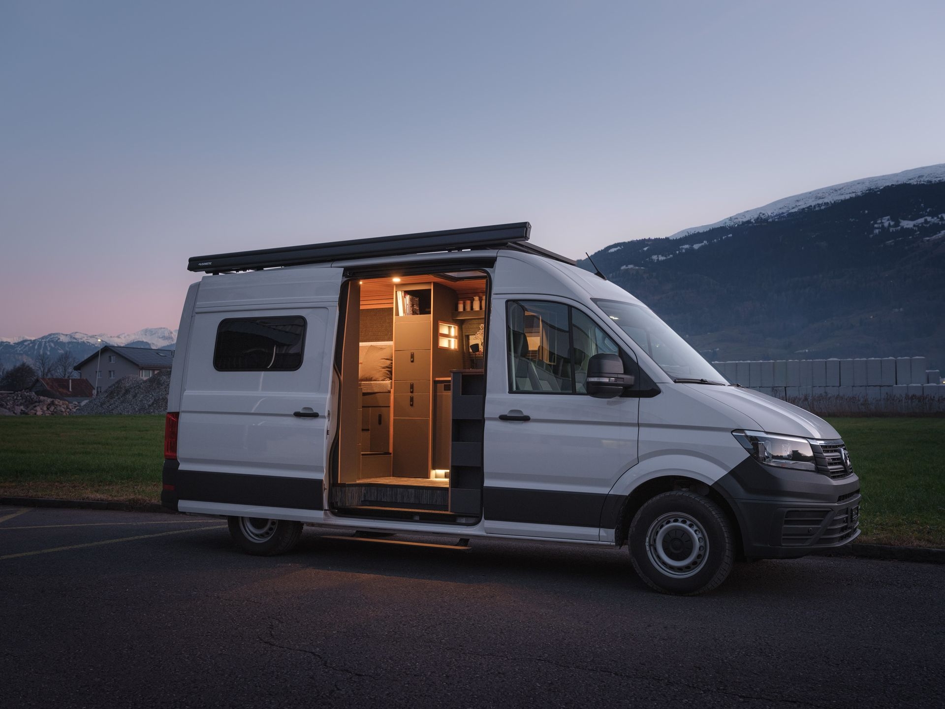 Aussenansicht von VW Crafter 4Motion mit Innenraumbeleuchtung. Seitliche Ansicht mit Seitentüre geöffnet und Einstiegstufe von Alphadynamik ausgefahren.