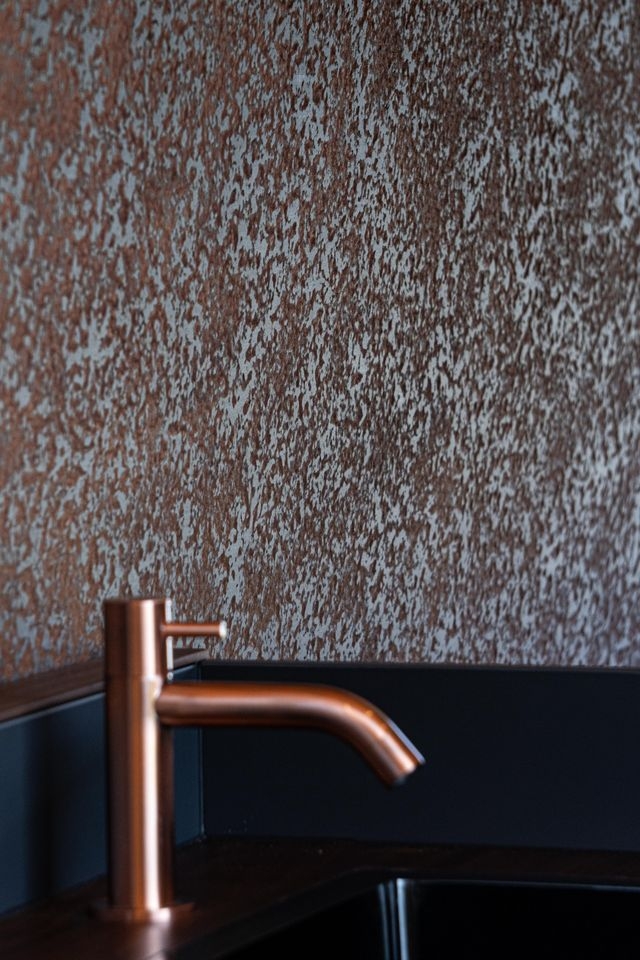 Bronzefarbener Wasserhan. Hat fast die gleiche Farbe wie die Wandbeplankung aus Leichtbauplatte Rostimitat. Die Arbeitsplatte im Camper Van von Cocoon Vans ist aus amerikanischem Nussbaum die Fronten sind dunkelgrau lackiert.