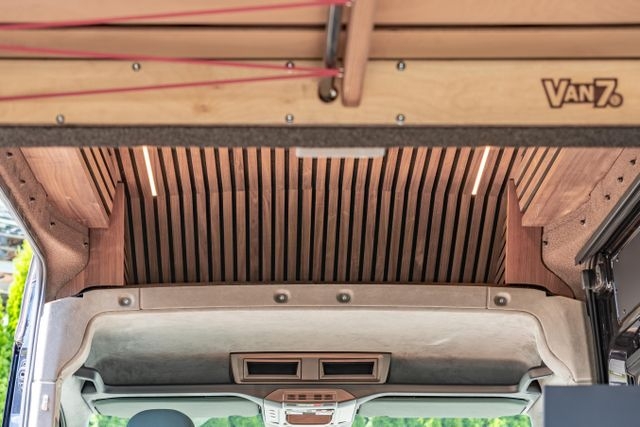 Blick vom Heck in den Bereich oberhalb der Autositze. Die Decke ist aus amerikanischem Nussbaum, beide seitentüren sind geöffnet und von hellbraun Sprükork eingerahmt. Der Ausbau wurde von Cocoon Vans umgesetzt.