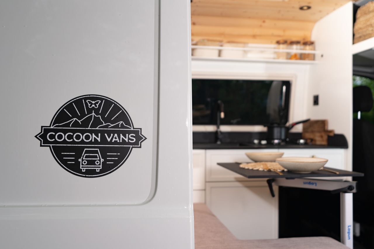 Cocoon Vans Logo an einer VW Crafter Schiebetüre. Im Hintergrund ist der Tisch für zwei Personen gedeckt